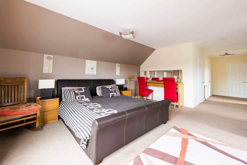 Spacious bedroom with dark leather bed, striped bedding, wooden furniture and geometric rug