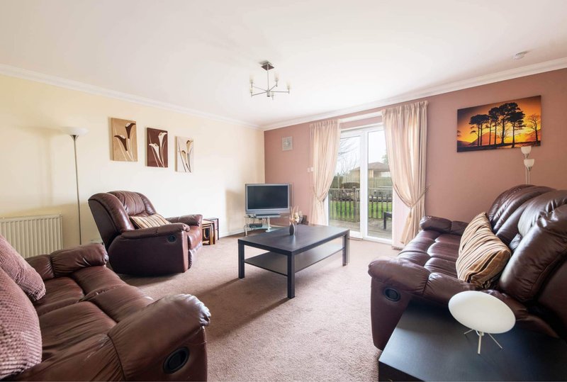 Spacious living room with brown leather recliners, TV, coffee table and garden views