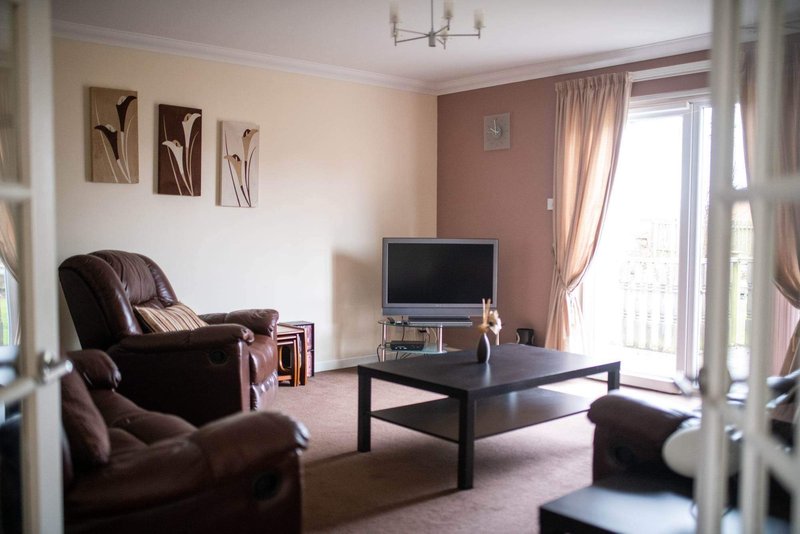 Living room with brown leather armchair, black coffee table, TV, and patio doors with curtains