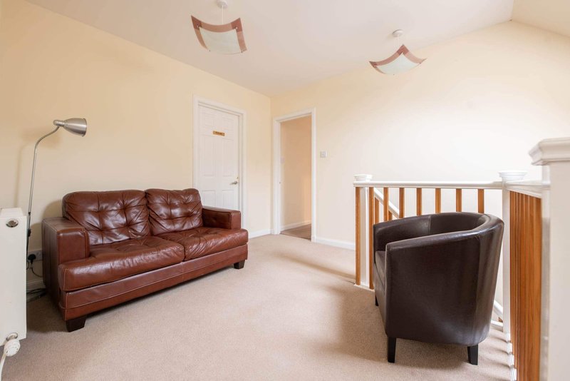 Bright living room with brown leather sofa, armchair, floor lamp and doorways