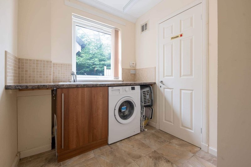 Utility room with washing machine, wooden cabinetry, sink and window with garden view