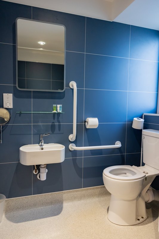 Accessible bathroom with blue tile walls, wall-mounted sink, grab bars, and toilet