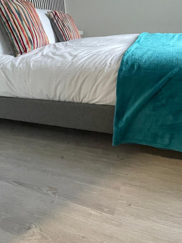 Bedroom with made double bed, striped pillows, turquoise throw, wooden floor