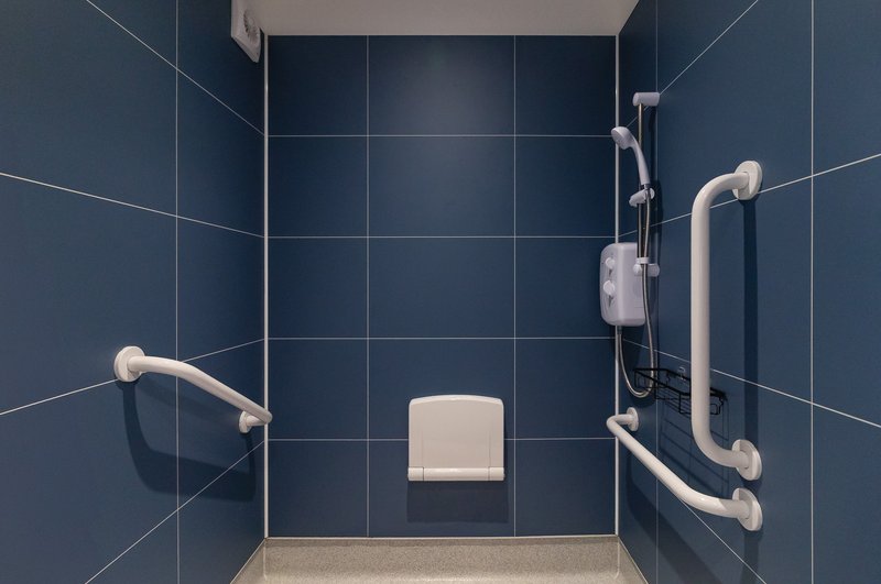 Accessible shower room with dark blue tiled walls, grab bars, and white seat.