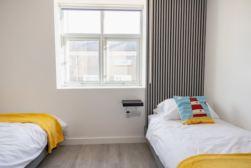 Twin bedroom with two beds, colorful pillows, yellow throws, and large window with radiator.