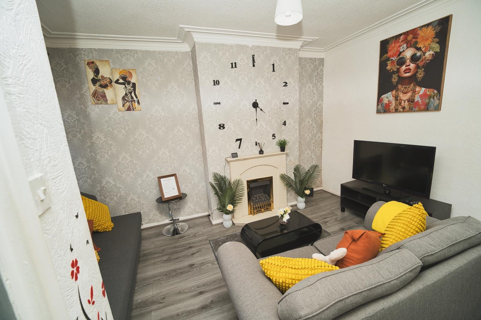 Living room with gray sofa, fireplace, wall clock, TV, and decorative artwork