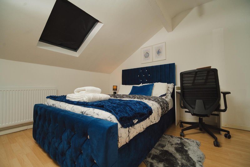 Bedroom with blue upholstered bed, white bedding, wooden floor, desk chair and skylight