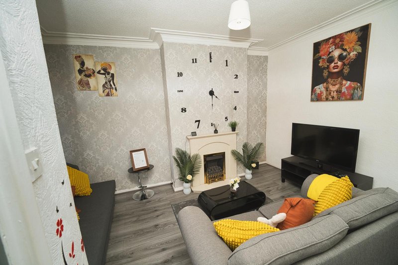 Compact living room with gray sofa, fireplace, wall clock, framed artwork and TV