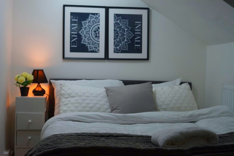 Bedroom with grey bed, pillows, bedside lamp, and framed wall art above