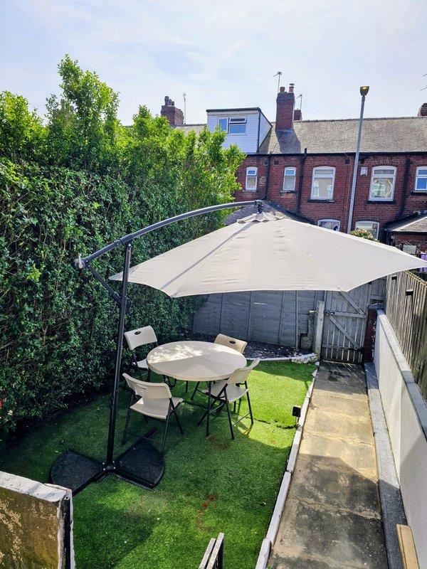 Sunny garden with table, chairs, cream parasol and hedging, terrace and brick townhouse