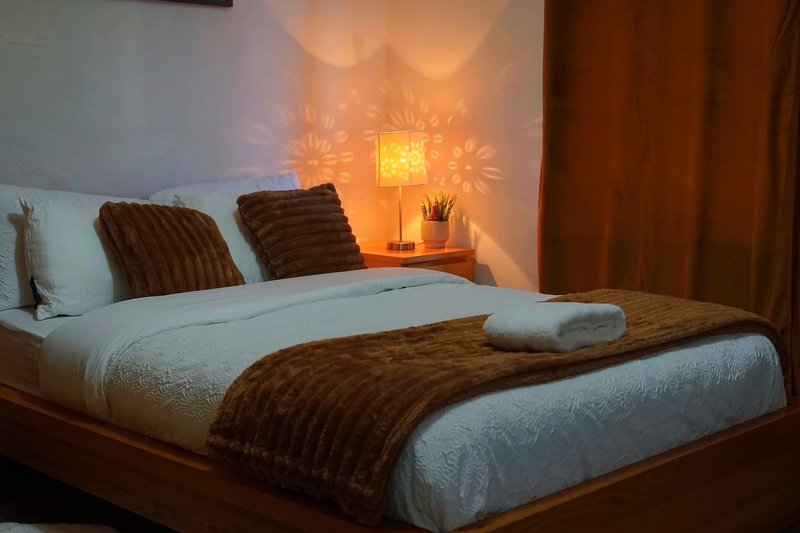 Bedroom with double bed, brown cushions, white bedding, and warm table lamp lighting