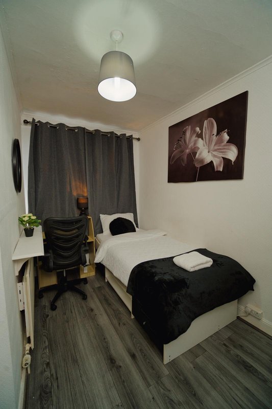 Compact bedroom with single bed, desk, office chair and wall-mounted floral artwork