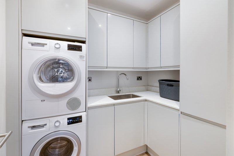 Compact laundry room with stacked white washer and dryer, white cabinetry and sink
