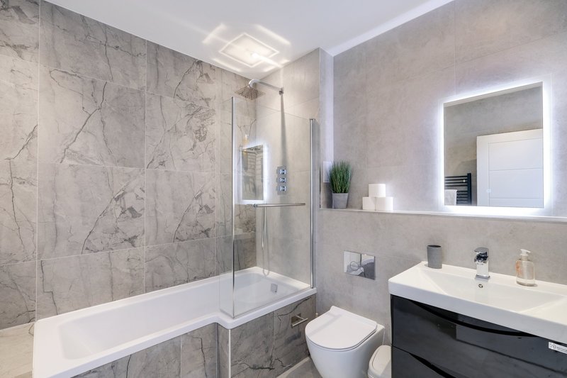 Modern bathroom with marble tiles, walk-in shower, toilet, and illuminated mirror vanity