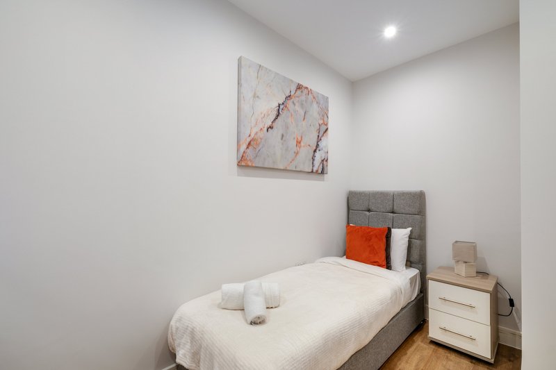 Modern bedroom with single bed, gray headboard, orange accent pillow, wooden nightstand and wall art