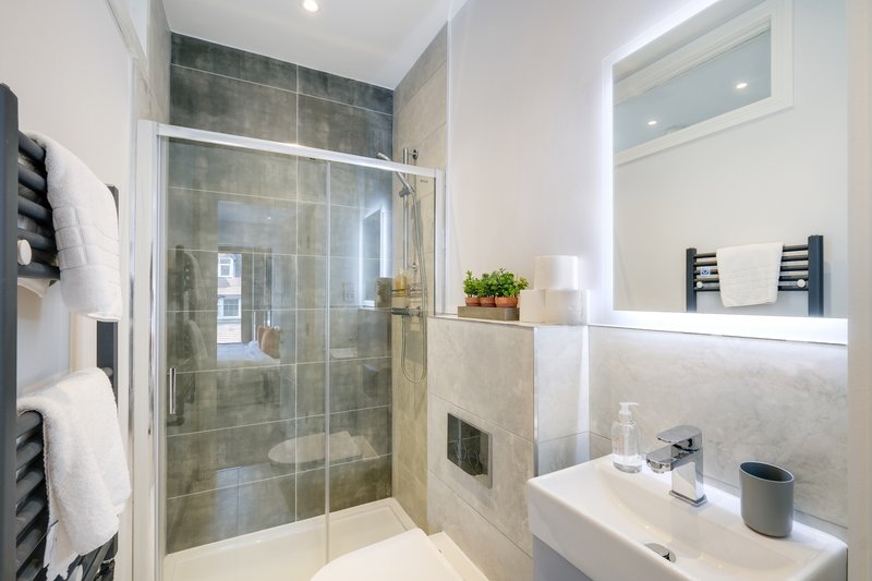 Modern bathroom with walk-in shower, white vanity sink, mirror and heated towel rails