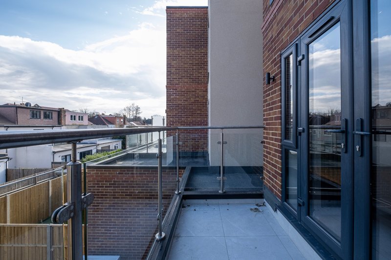 Modern brick building exterior with rooftop terrace, glass doors and metal railings