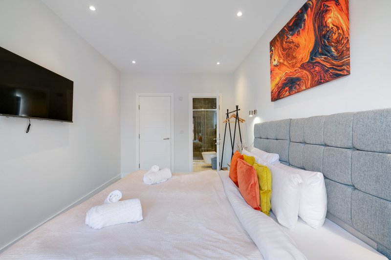 Modern bedroom with double bed, gray upholstered headboard, wall-mounted TV, and colorful artwork