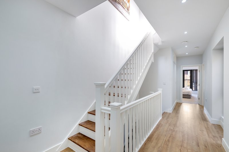 Bright staircase with white railings, wooden steps, and light wood flooring throughout hallway