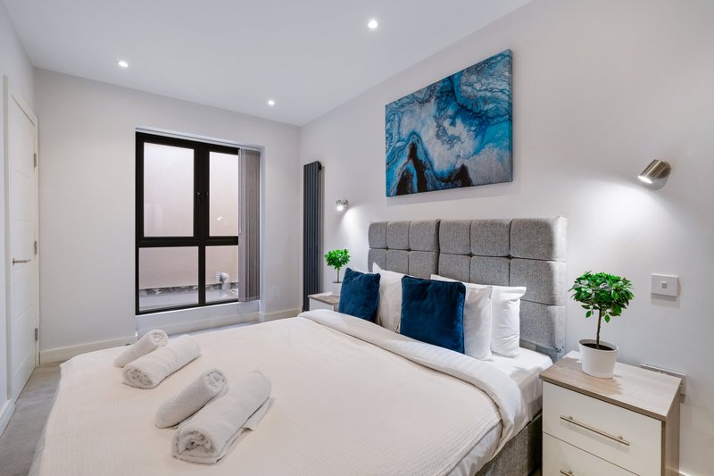 Modern bedroom with double bed, grey headboard, blue artwork, and black-framed window