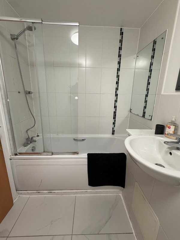 Modern bathroom with white tiles, glass shower enclosure, white sink and black towel