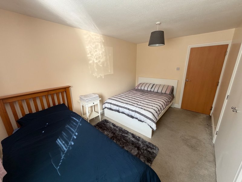 Shared bedroom with two single beds, wooden headboards, pendant lamp, and cream walls