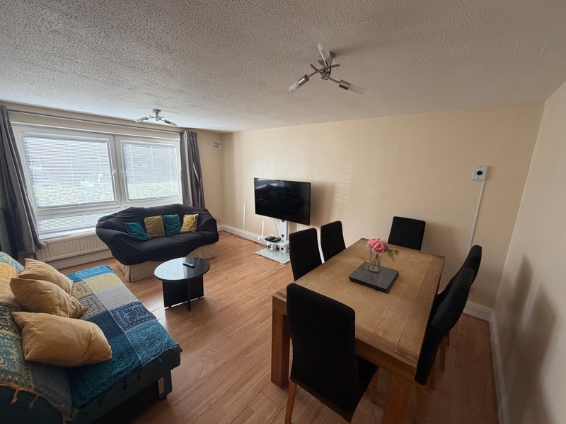 Living room and dining area with sofa, armchairs, wooden dining table, TV, and large windows