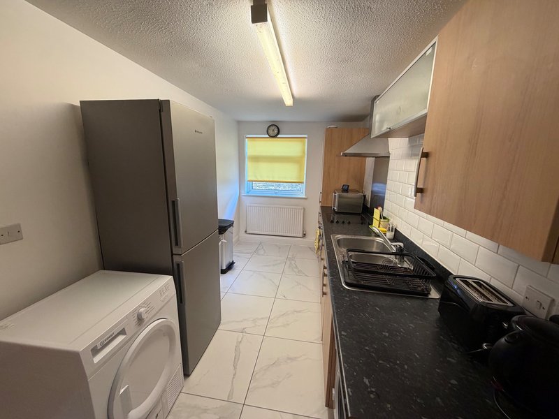 Galley kitchen with appliances, black countertop, white tiles and laundry area