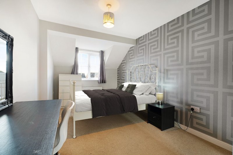Modern bedroom with double bed, geometric wallpaper, wooden desk, and warm lighting