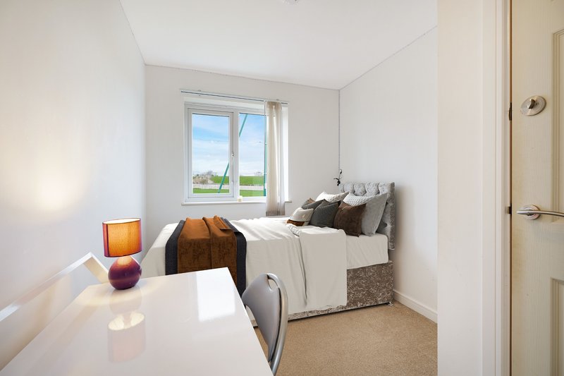 Bright bedroom with single bed, desk, window overlooking green landscape, and warm lighting