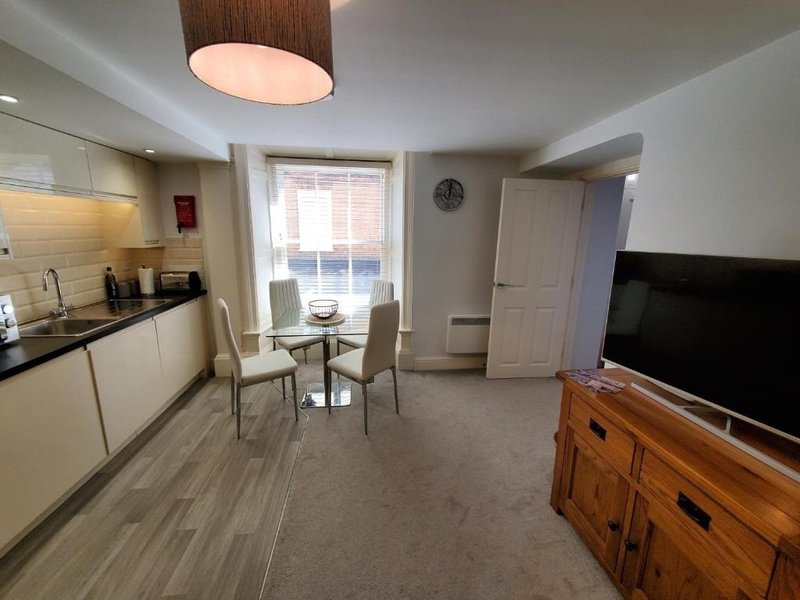 Open-plan kitchen and living area with dining table, wooden TV stand, and bright window
