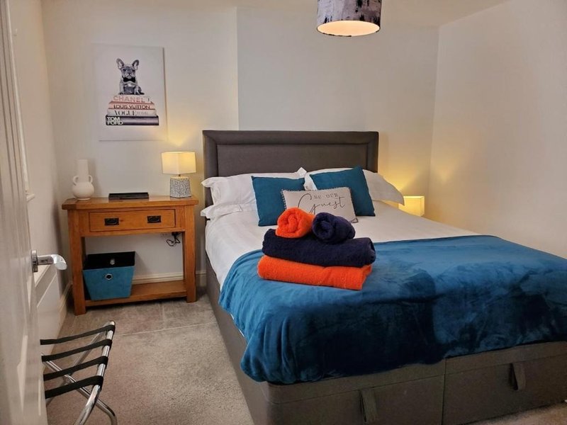 Bedroom with double bed, blue bedding, wooden nightstand, wall art, and pendant lighting