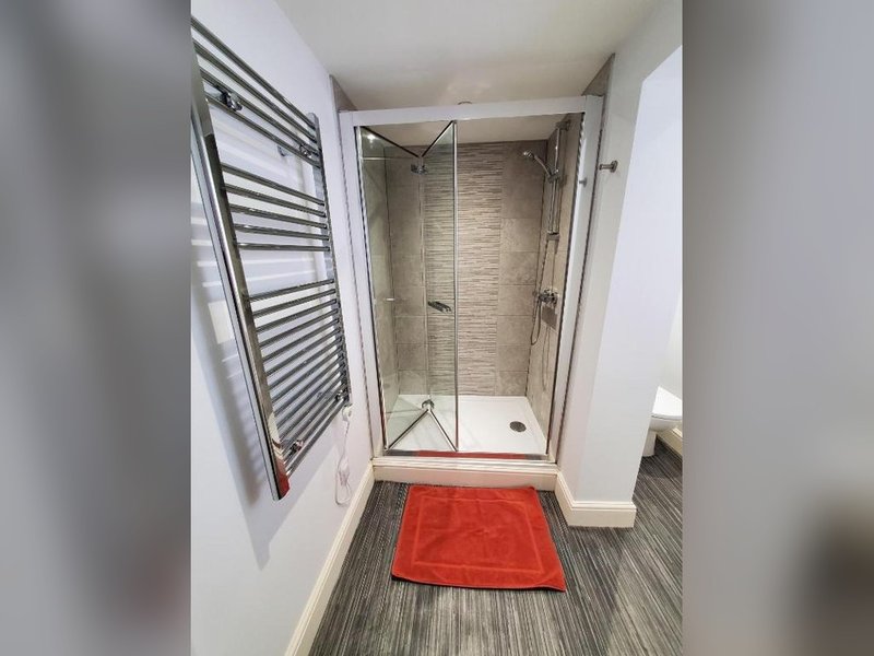 Modern bathroom with walk-in shower, heated towel rail, and red bath mat