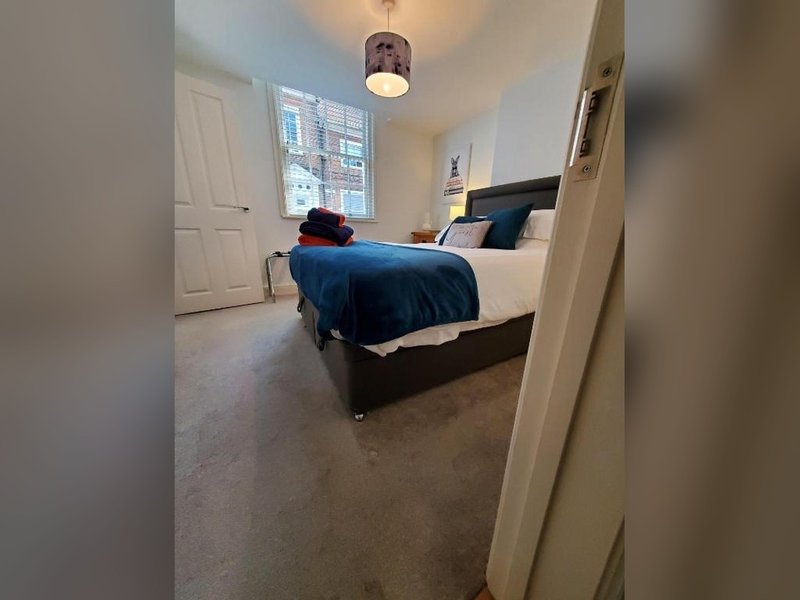 Spacious bedroom with double bed, blue bedding, pendant light, and carpet flooring