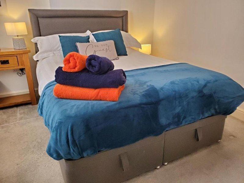 Modern bedroom with blue duvet, grey upholstered headboard, and folded towels on bed