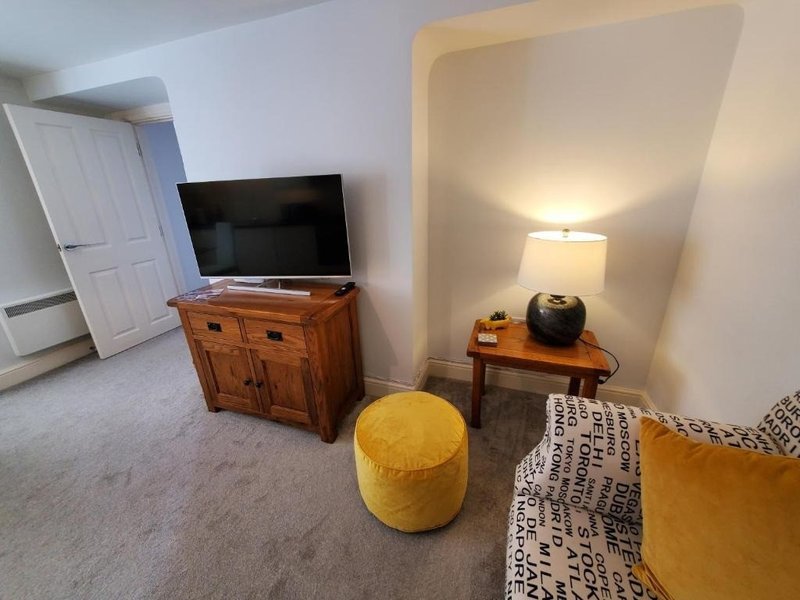 Living room with TV on wooden cabinet, yellow ottoman, lamp, and patterned rug