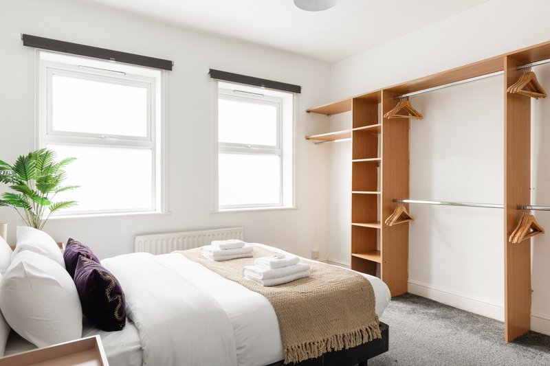 Bright bedroom with double bed, wooden wardrobe, windows and potted plant