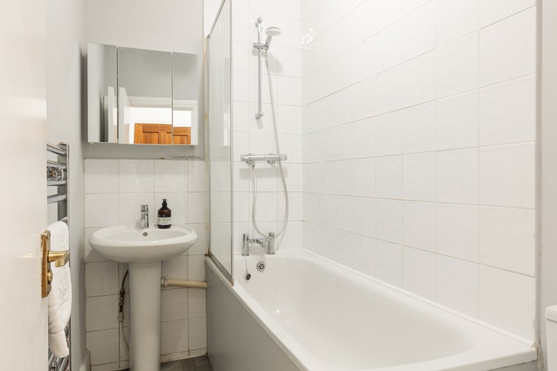 Clean modern bathroom with pedestal sink, bathtub, shower, mirror cabinet and white tile walls
