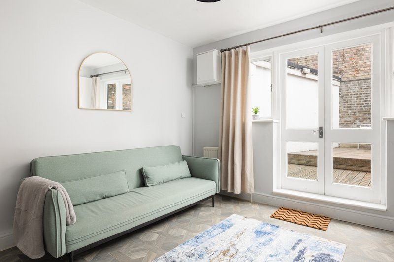 Bright living room with green sofa, round mirror, patio doors and wooden flooring