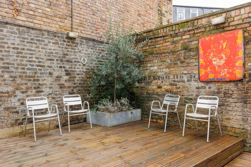 Brick courtyard with wooden decking, white metal chairs, potted plant, and wall art