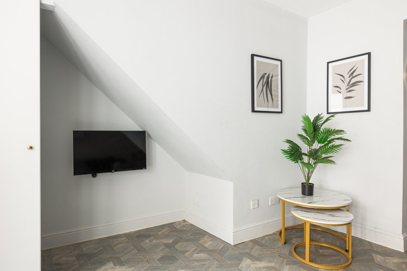 Attic bedroom with wall-mounted TV, potted plant, framed botanical prints and wooden side table
