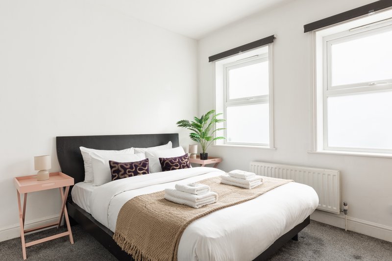 Bright bedroom with double bed, black headboard, white bedding, and two windows
