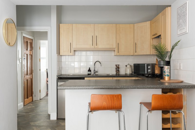 Modern kitchen with wooden cabinets, grey countertop, white tile backsplash and orange bar stools