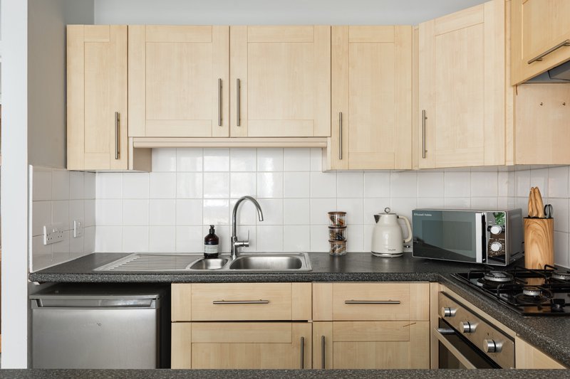 Modern kitchen with light wood cabinets, black countertops, stainless steel appliances and white tile backsplash