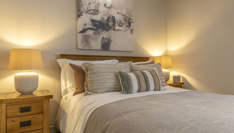 Modern bedroom with double bed, wooden headboard, bedside tables, warm lighting and abstract wall art