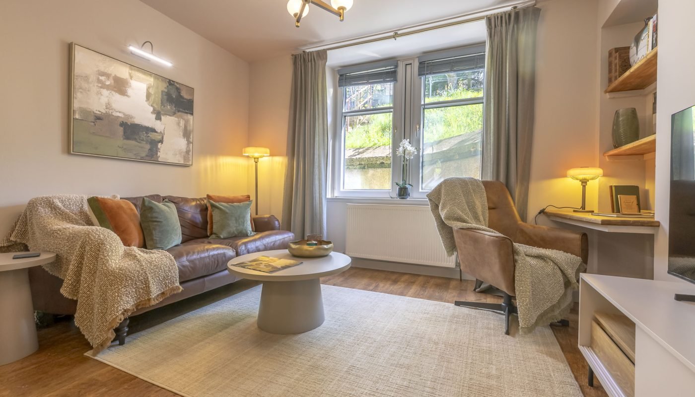 Bright living room with sofa, armchair, coffee table, shelving and large windows