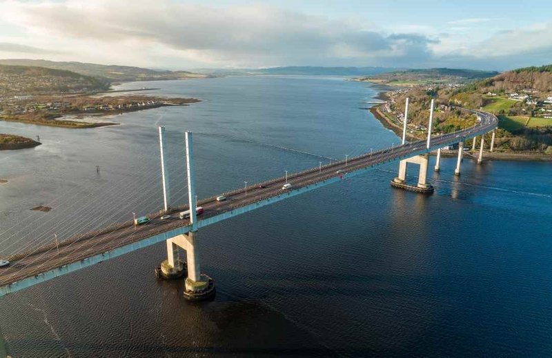 Aerial view of large cable-stayed bridge spanning blue water with coastal landscape and hills
