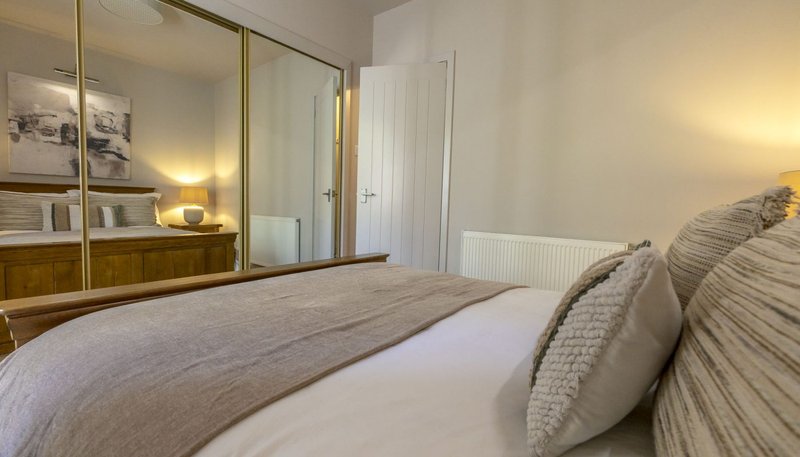 Bright bedroom with double bed, mirrored wardrobe, bedside lamp and radiator