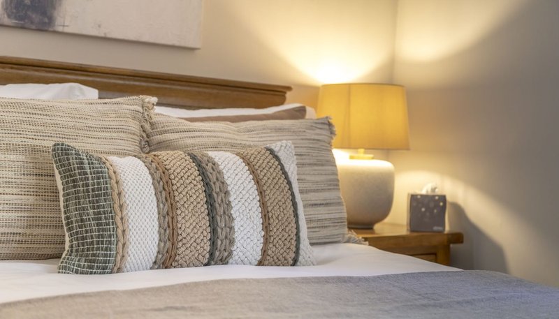 Bedroom with double bed, striped pillows, wooden headboard and bedside lamp