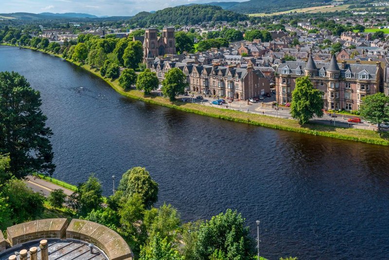 Aerial view of riverside town with historic stone buildings, river, and surrounding hills